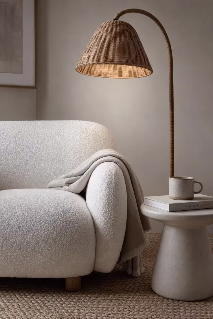 12 Cute Living Room Ideas for Apartments That Feel Like Home 2 Close-up of a white boucle armchair next to a rattan floor lamp in a calm apartment corner with cool morning light.
