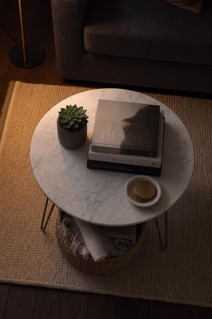 12 Cute Living Room Ideas for Apartments That Feel Like Home 10 Overhead view of a petite round marble coffee table with woven basket storage beneath in moody low apartment light.