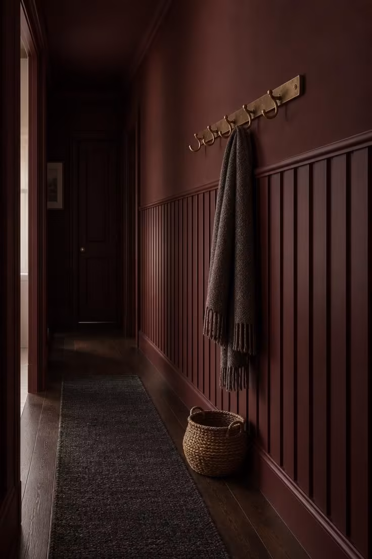 14 Warm Dark Hallway Ideas to Make a Bold Statement 12 Narrow corridor with vertical battens painted deep oxblood to dado height, an aged brass hook rail, and a low woven basket on the floor.