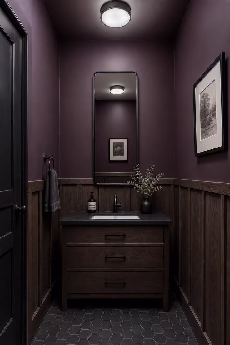 Smoked oak wainscoting below deep plum walls in a dark moody powder room with white porcelain sink