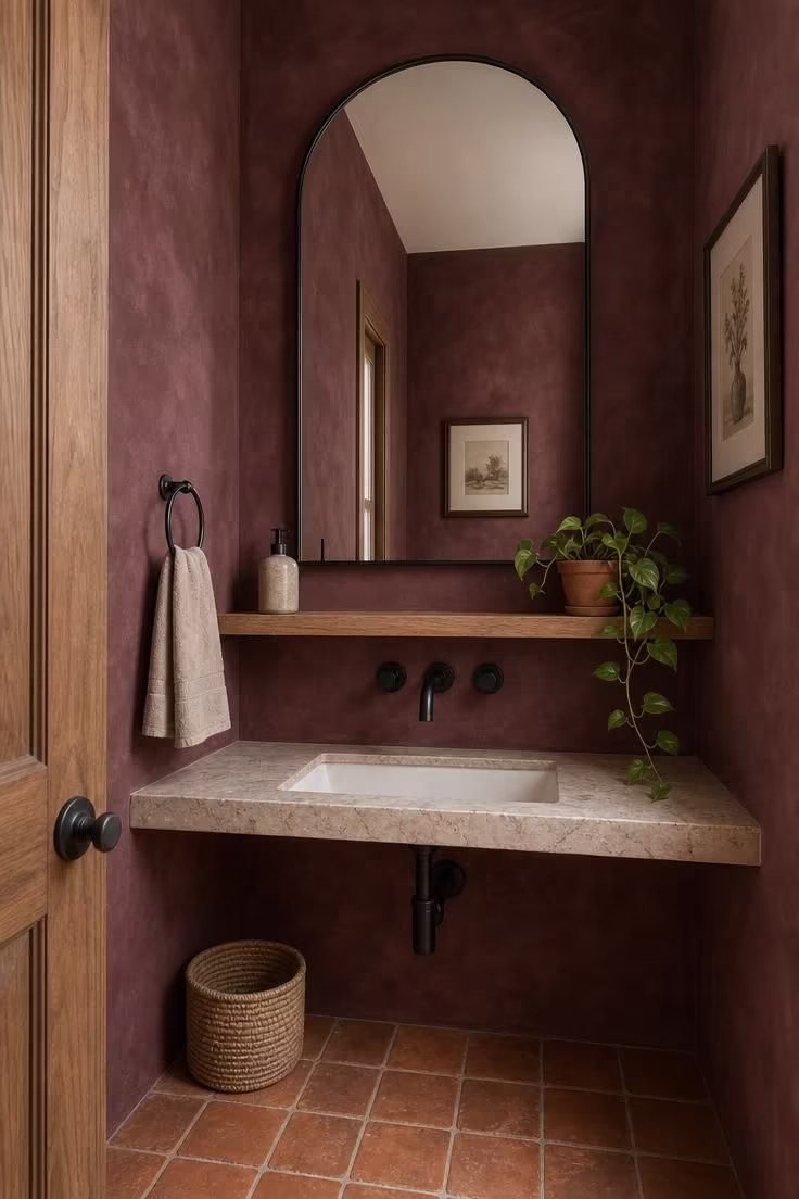 Oversized arched mirror on burgundy limewash wall in dramatic powder room with terracotta floor
