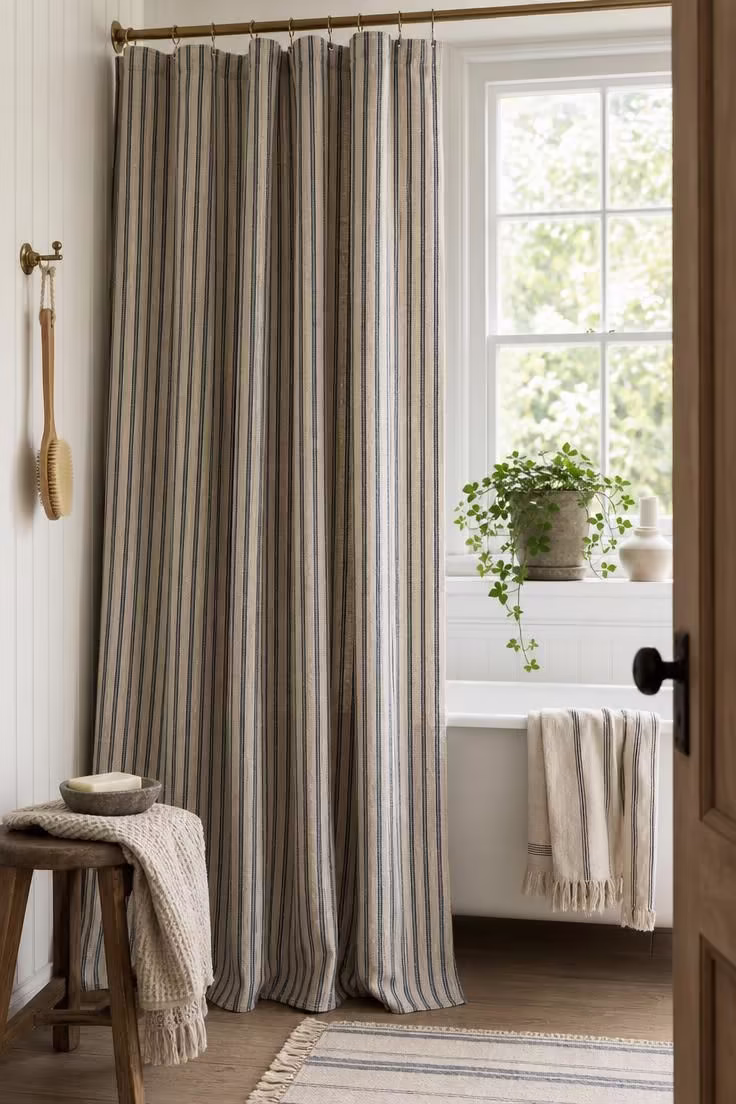 14 Eclectic Bathroom Ideas for a Space Full of Character 9 A floor-length ticking-stripe linen shower curtain in faded indigo and cream on a brass rod.