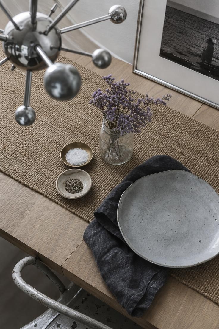 14 Warm Eclectic Dining Room Ideas That Feel Like Home 7 An overhead detail of a modern eclectic dining room table with a white-oak slab, woven seagrass mat, brass and ceramic salt dishes, dried sea lavender, and a chrome Sputnik pendant.