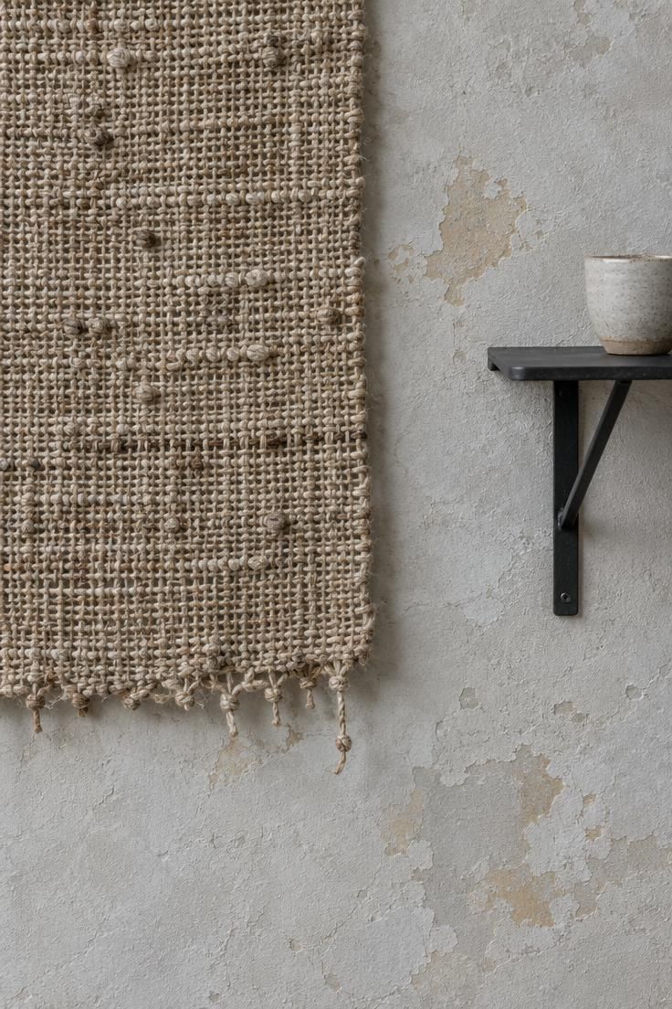 13 Warm Eclectic Home Office Ideas for Historic Rooms 12 A handwoven fiber wall hanging against aged plaster beside the end of a slim black metal shelf.
