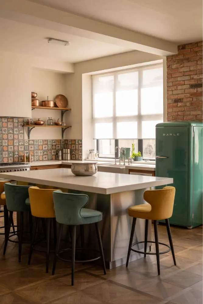 32 Eye-Catching Eclectic Kitchen Design Ideas to Love 10 Stylish eclectic kitchen with brushed-steel island, white quartz countertop, velvet teal and mustard yellow bar stools, patterned ceramic backsplash, and vintage emerald-green refrigerator