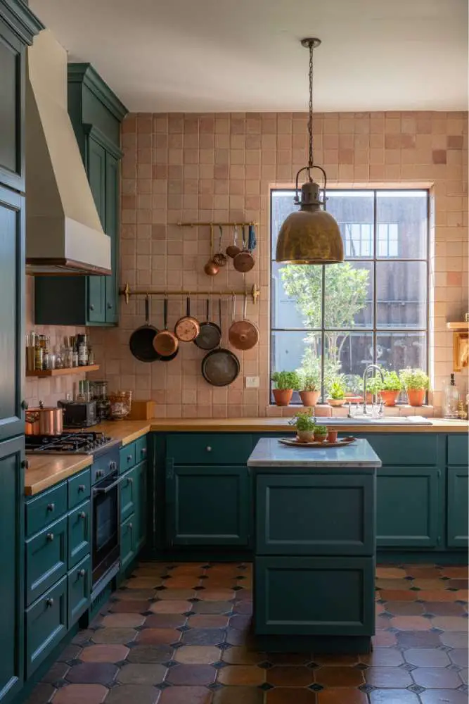 32 Eye-Catching Eclectic Kitchen Design Ideas to Love 13 Stylish eclectic kitchen with dark teal cabinetry, butcher block countertop, handcrafted terracotta tile backsplash, brass pendant light, and marble-topped island