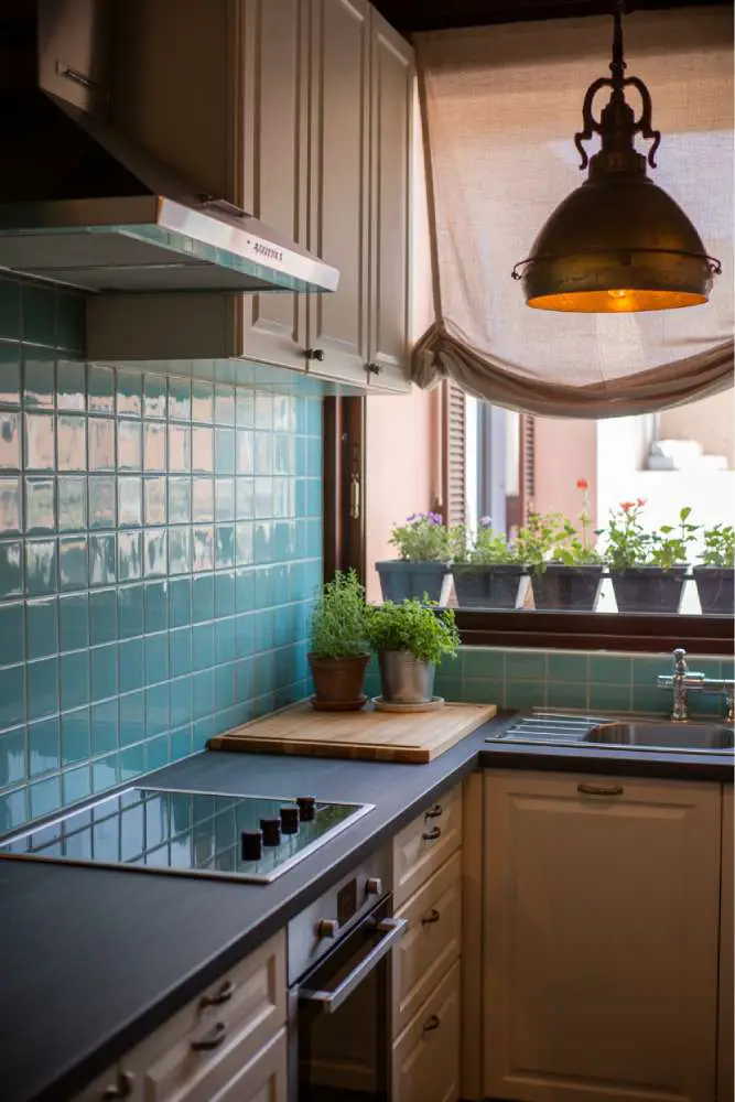 32 Eye-Catching Eclectic Kitchen Design Ideas to Love 21 Modern eclectic small kitchen with turquoise geometric tile backsplash, white cabinetry, dark gray countertops, brass pendant light, and butcher-block island