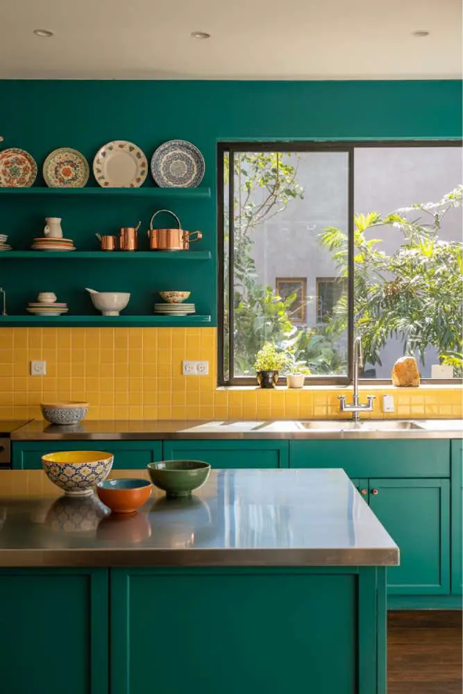 32 Eye-Catching Eclectic Kitchen Design Ideas to Love 26 Modern eclectic kitchen with vibrant teal cabinets, yellow tile backsplash, stainless steel island, dark grey granite countertop, and colorful ceramic bowls