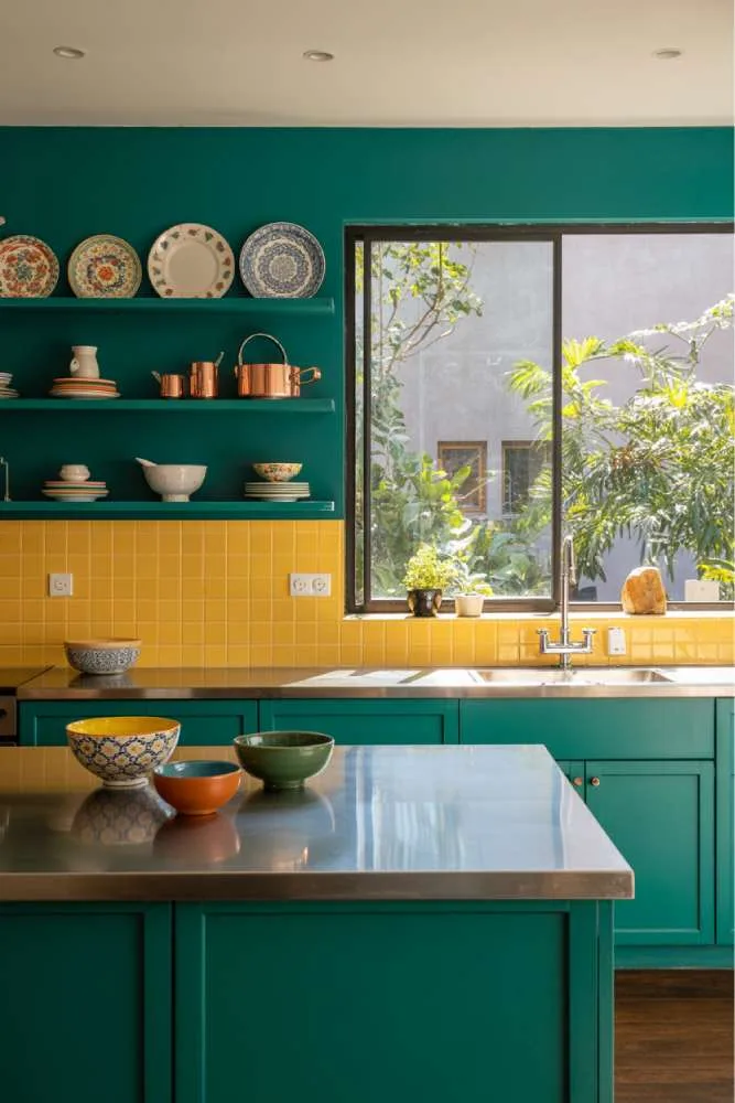 32 Eye-Catching Eclectic Kitchen Design Ideas to Love 26 Modern eclectic kitchen with vibrant teal cabinets, yellow tile backsplash, stainless steel island, dark grey granite countertop, and colorful ceramic bowls