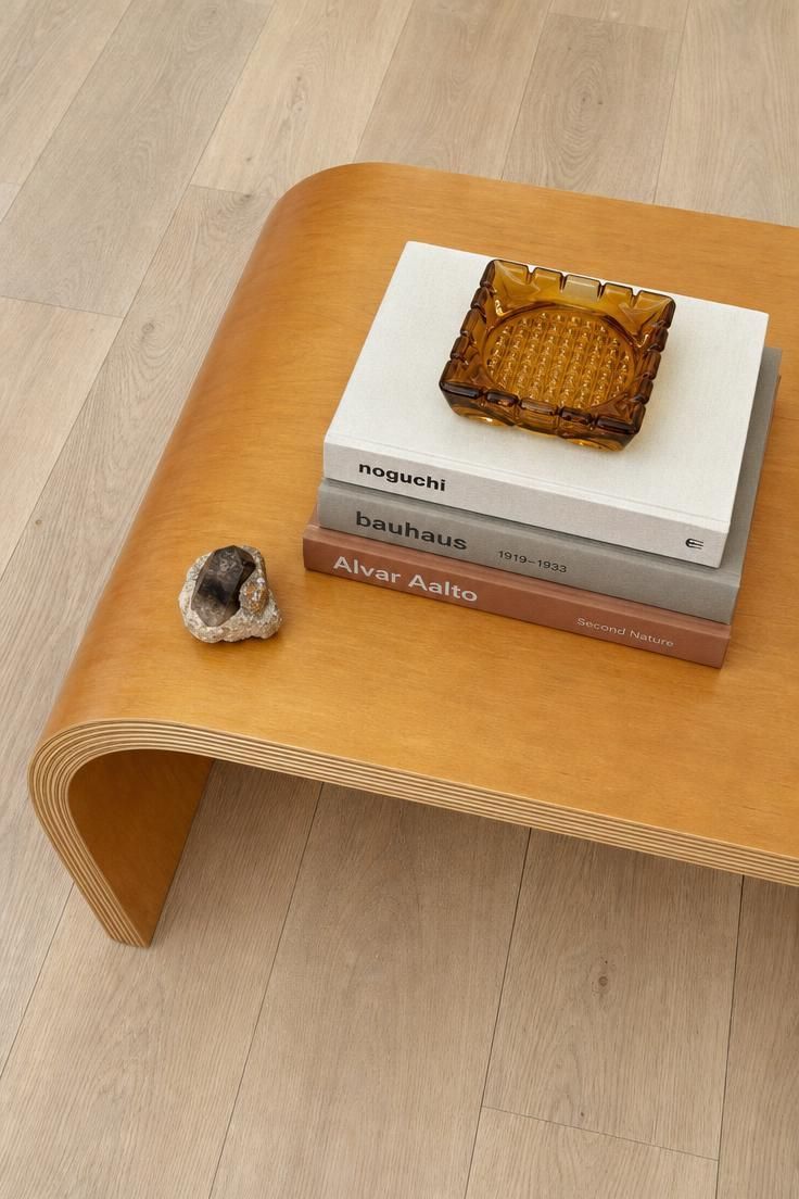13 Eclectic Mid Century Modern Ideas for Warm Lived-In Rooms 5 Overhead view of a honey bentwood coffee table with art books, an amber glass ashtray, and a small mineral specimen on pale oak floor.