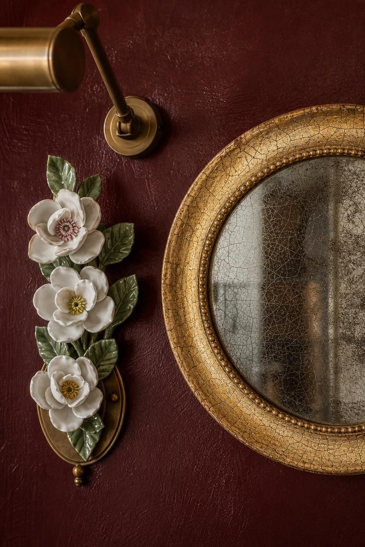 11 Warm Eclectic Wall Decor Ideas You Will Love Now 6 A close view of a crackled gilt mirror and a porcelain botanical spray on a deep oxblood wall.