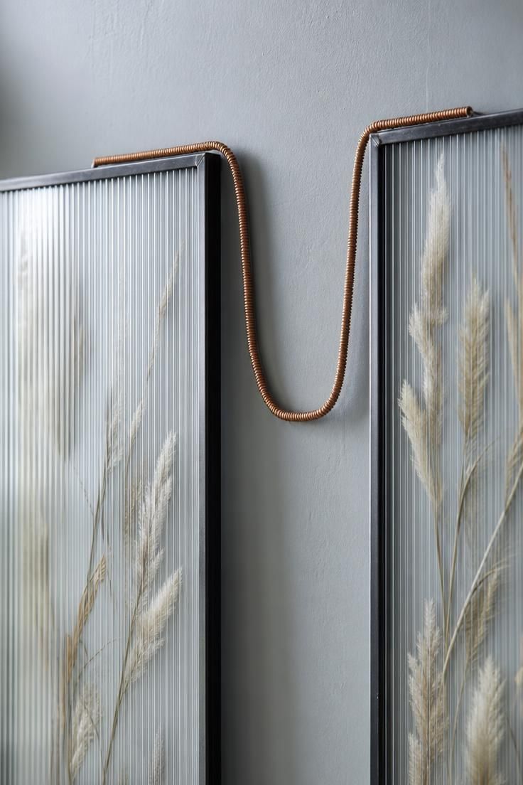 11 Warm Eclectic Wall Decor Ideas You Will Love Now 9 Two vertical reeded-glass frames holding pale pressed grasses, connected by a hand-coiled copper wire on a soft gray wall.