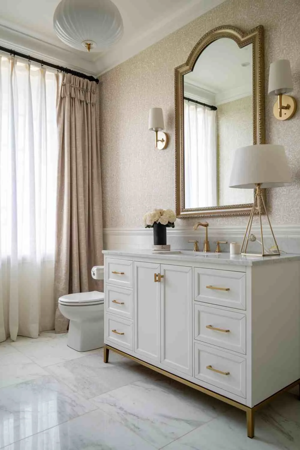 21 Elegant Bathroom Design Ideas for a Luxurious Look 2 Elegant bathroom with white vanity featuring gold hardware, marble countertop, gold lamp, white and gray marble tile flooring, beige patterned wallpaper, and gold-framed mirror