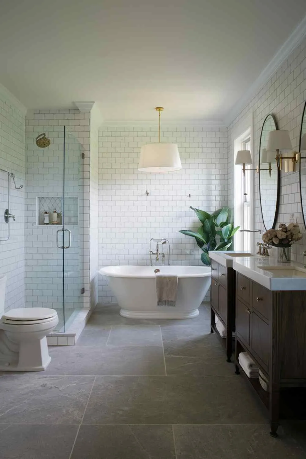 21 Elegant Bathroom Design Ideas for a Luxurious Look 10 Contemporary bathroom with freestanding bathtub, separate shower, toilet, double vanity with dark wood, white tiled walls, gray tiled floor, white lampshade over bathtub, and potted plant near window