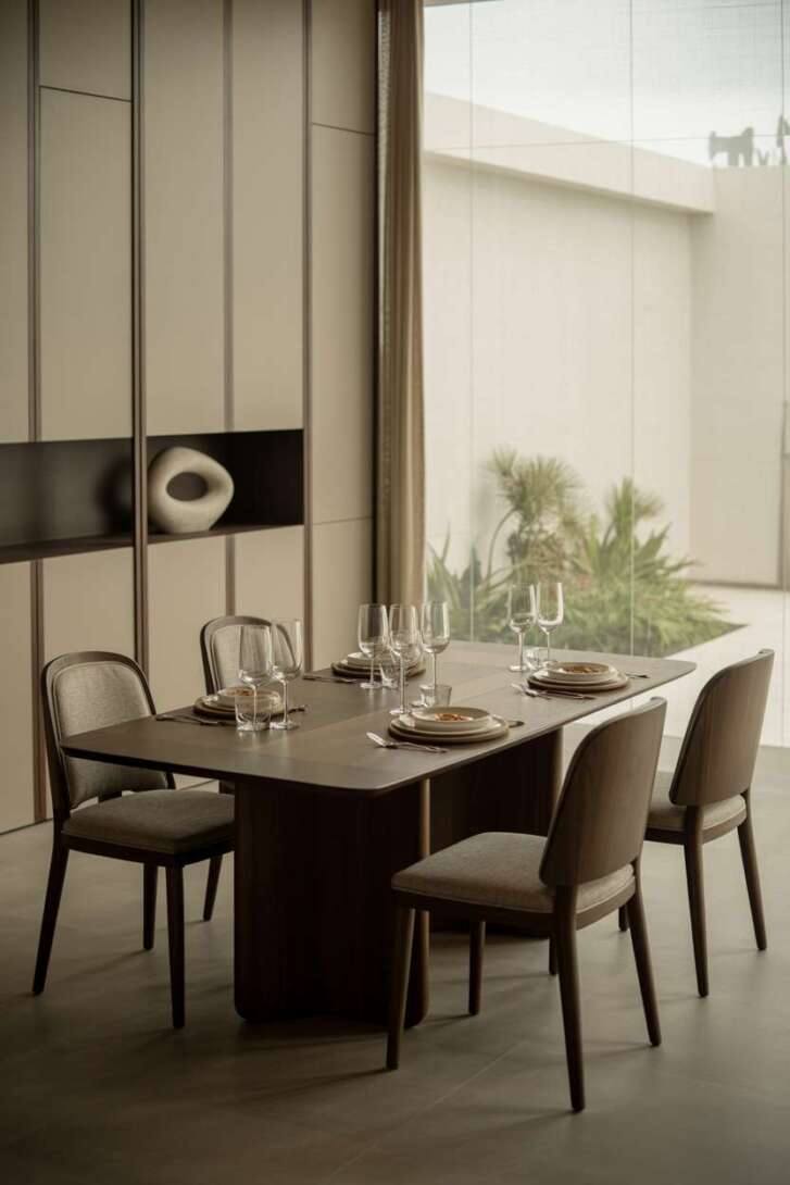 Modern dining room with rectangular walnut table, light grey chairs, and built-in storage topped with abstract sculpture