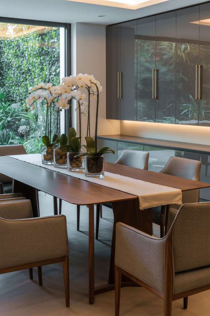 Modern dining room featuring walnut table with grey chairs and built-in storage with grey lacquered cabinets and brass handles