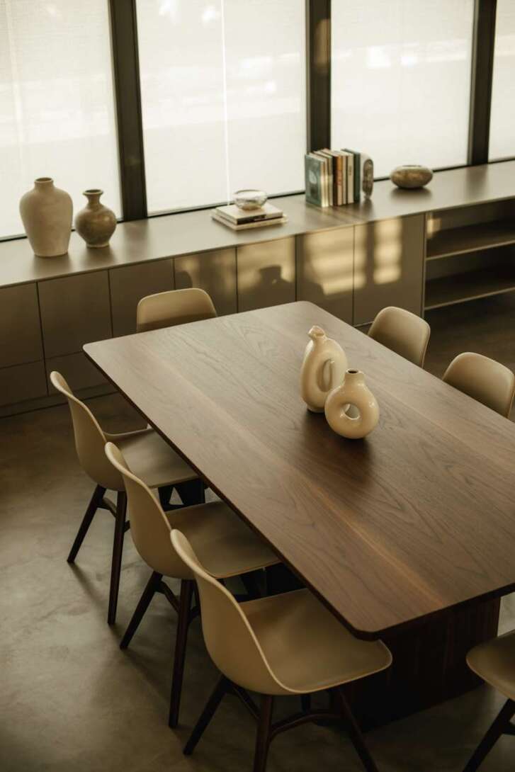 Modern dining room with dark walnut table, cream molded plastic chairs, and built-in storage with brushed nickel finish