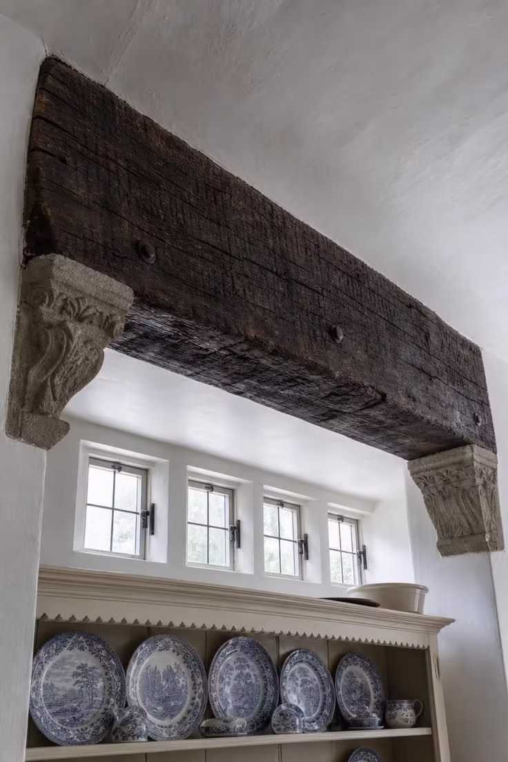 19 English Cottage Kitchen Ideas Full of Old World Charm 12 Reclaimed oak ceiling beam with stone corbel brackets spanning a cottage kitchen above a cream dresser with transferware plates.