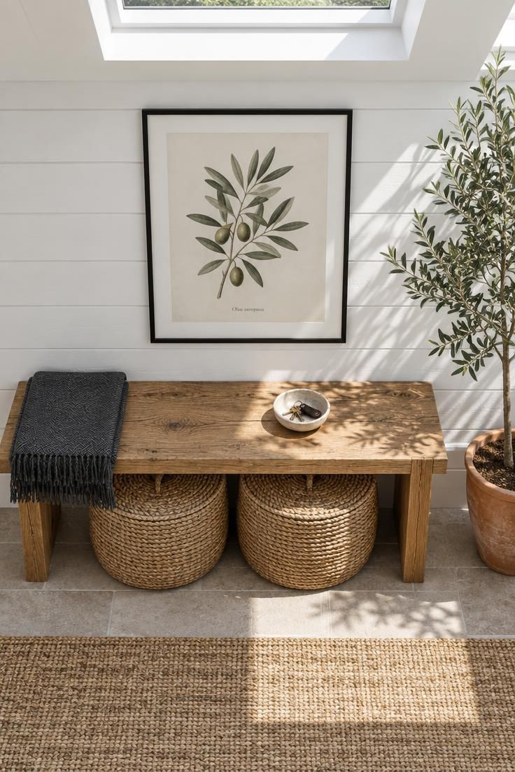 Entryway Bench Styling for a Practical and Finished Look 3 Overhead view of a reclaimed oak bench with two lidded seagrass baskets underneath, a framed botanical print above, an olive tree beside, and bright midday light.
