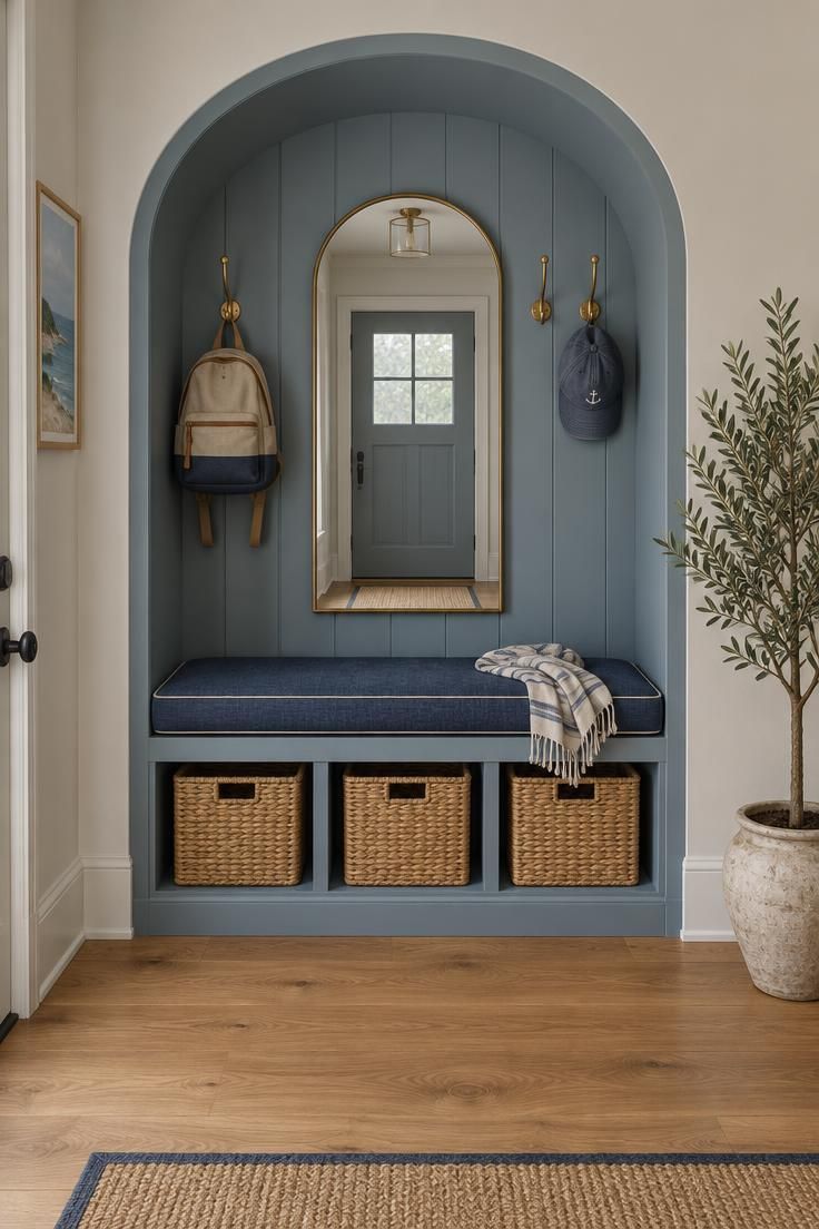 11 Warm Entryway Command Center Ideas for a Calmer Drop Zone 6 Muted blue built-in bench in an arch alcove with basket storage, brass hooks, and an arched mirror.