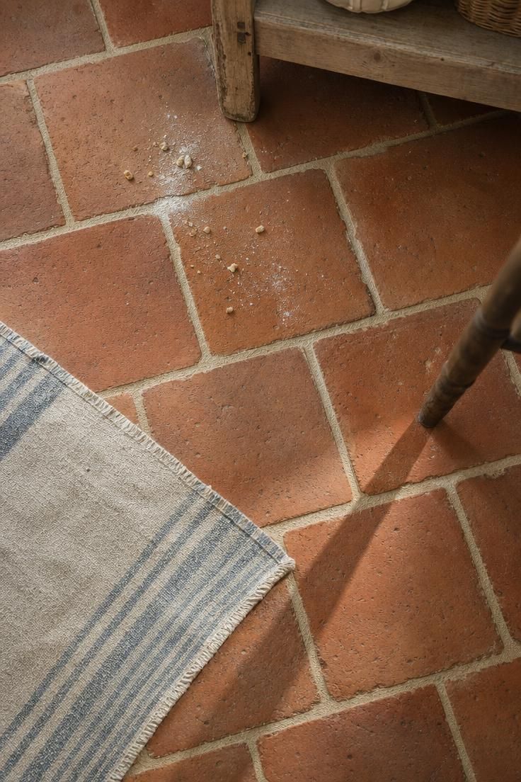 Overhead view of unglazed terracotta floor tiles in a running bond pattern with natural color variation in a french cottage kitchen under cool morning light.