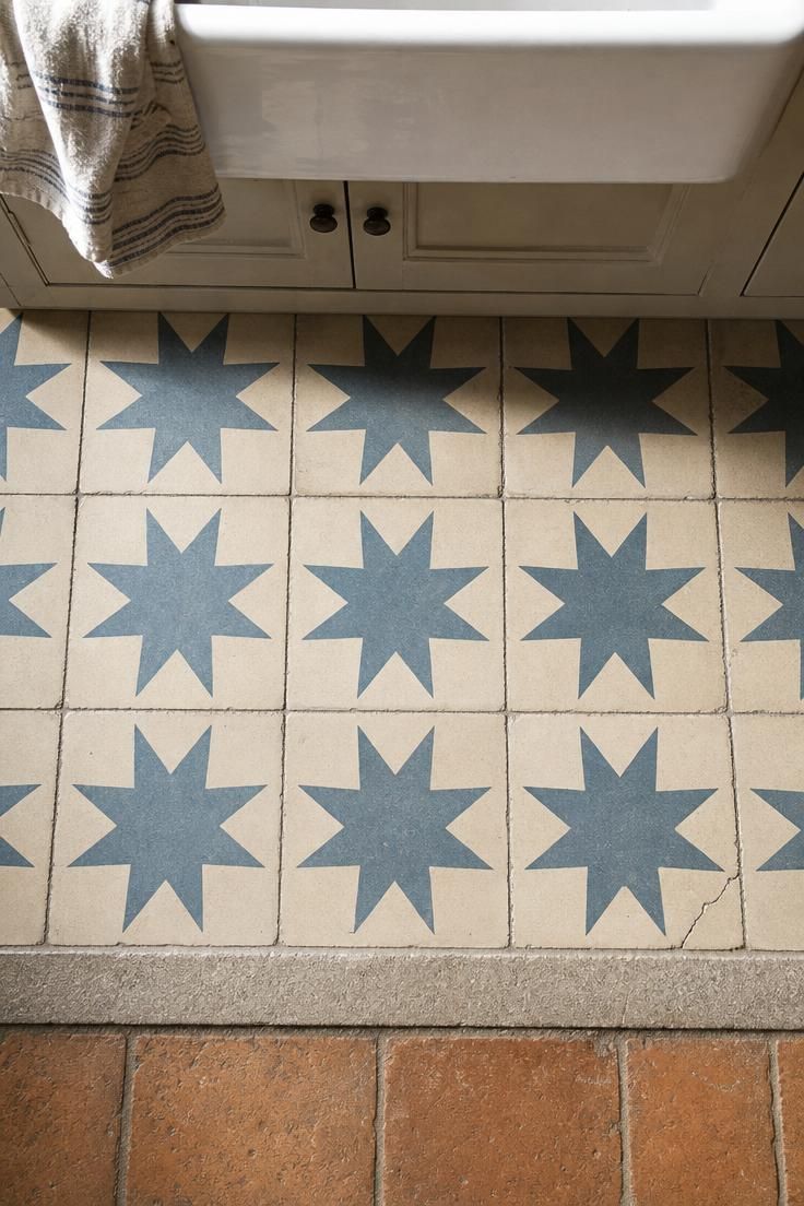 Handmade encaustic cement floor tiles in a blue and cream geometric star pattern as an accent strip in a french cottage kitchen under bright midday light.