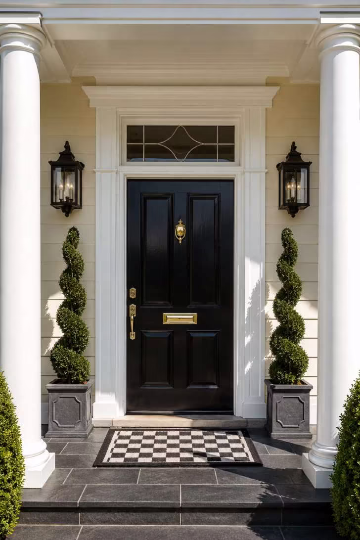 Symmetrical spiral boxwood topiaries in stone planters flanking a black front door