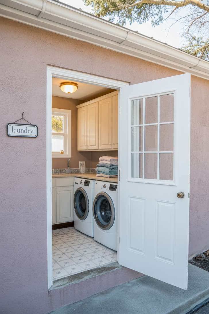 A fully enclosed built-in laundry room inside a garage with glass-panel door, white cabinets, and patterned tile floor
