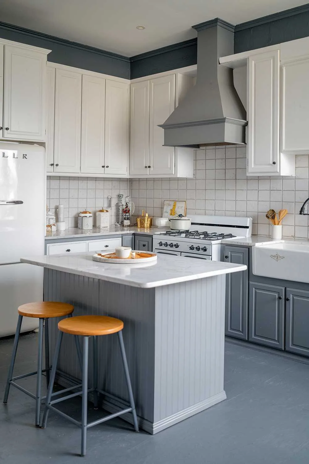 21 Inspiring Gray and White Kitchen Ideas for a Modern Look 1 A gray and white kitchen decor. There is a gray kitchen island with a white marble top and a few stools. There are white cabinets on the walls. There is a gray cabinet under the island. There is a white stove with four burners and a gray hood above it. There is a white refrigerator on the left. There is a white sink with a gray faucet on the right. The floor is gray.