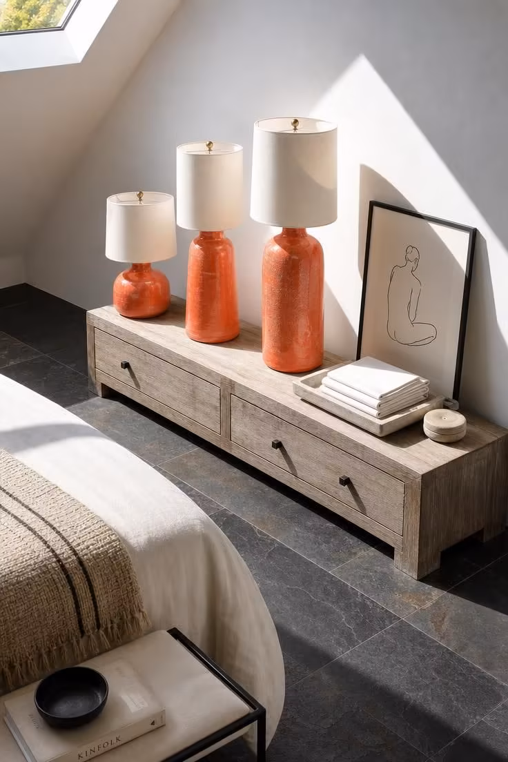 Three coral ceramic table lamps on a grey-washed console above dark slate floor tiles in bright midday light