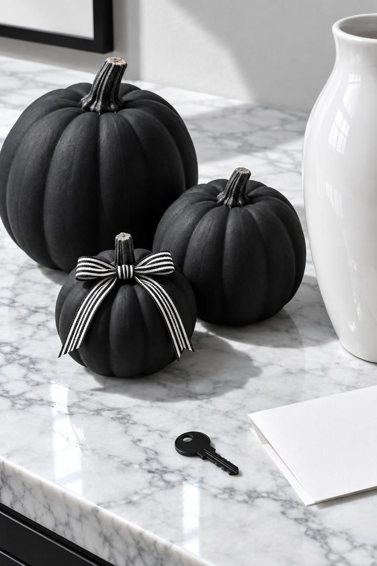 13 Cozy Halloween Aesthetic Ideas for a Warm Autumn Home 5 Matte black pumpkins with striped ribbon on a marble console with a white vase.