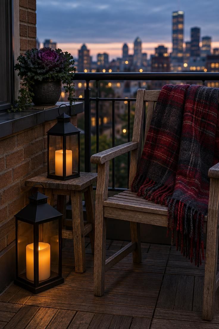 13 Cozy Halloween Apartment Decor Ideas for Small Spaces 10 Small apartment balcony at dusk with two black lanterns glowing amber, one on the deck and one on a stool, and a tartan throw draped over a teak chair.