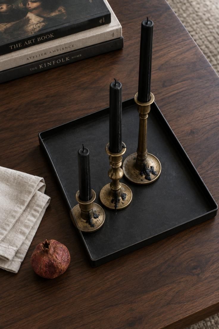 13 Cozy Halloween Apartment Decor Ideas for Small Spaces 13 Overhead view of a black metal tray holding three black taper candles in mismatched brass holders of varying heights on a walnut coffee table.