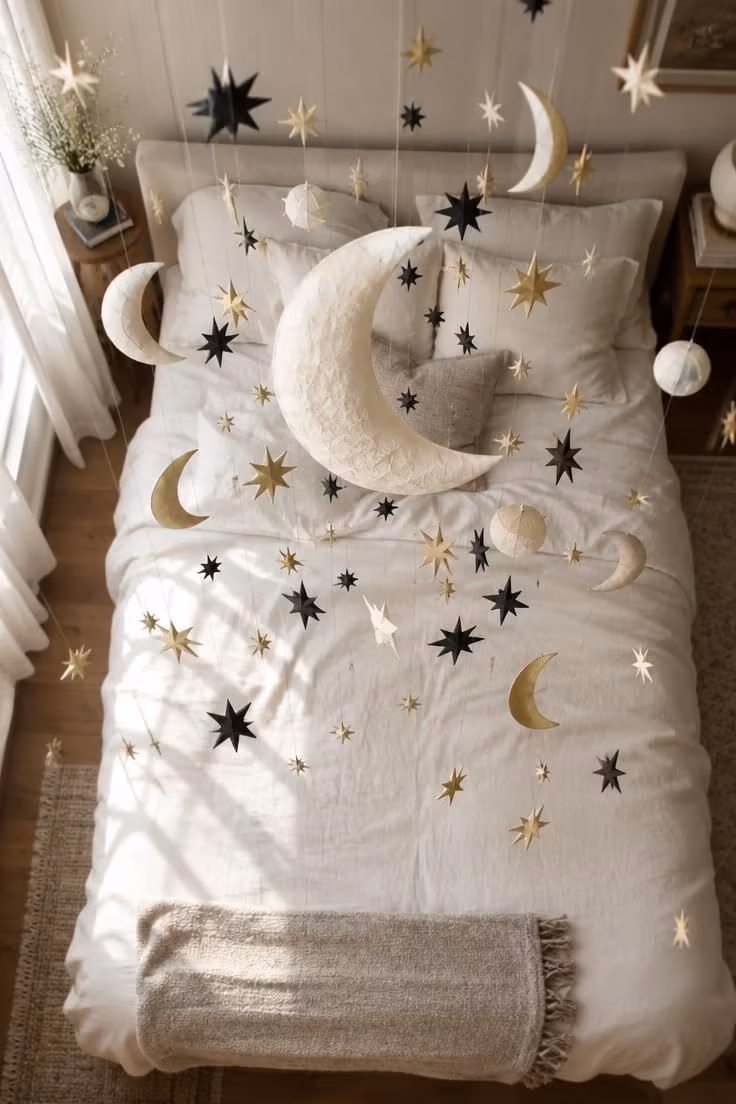 An overhead view of paper moons and stars suspended at different heights above a bed with pale bedding.