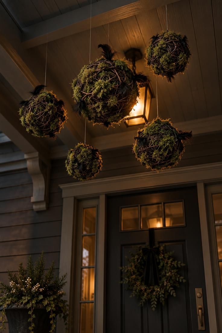 Cluster of twig and moss spheres hung from a porch ceiling at varied heights, glowing in front of a warm porch light.