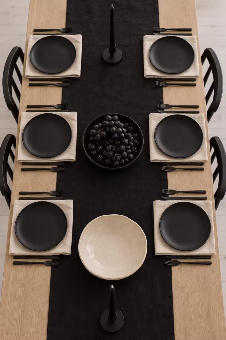11 Hauntingly Easy Halloween Party Decor Ideas for Home 10 A long table set entirely in matte black and bone tones, with black plates on bone napkins and a low dark centerpiece of dark fruit.