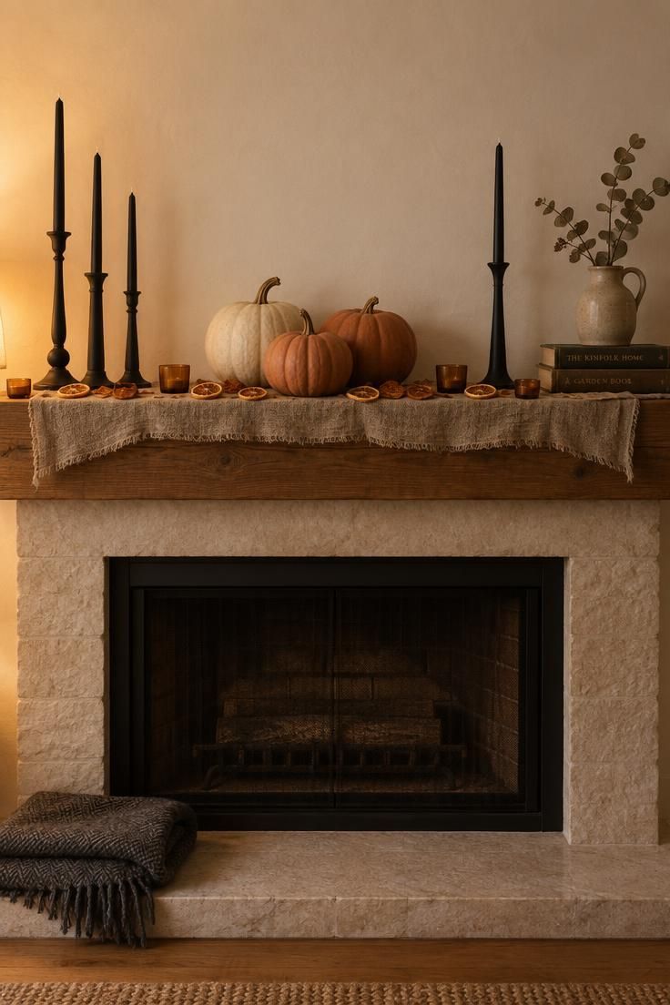 A living room mantel with tall black candlesticks at the back, cream and orange pumpkins in the middle, and tea lights with dried orange slices along the front edge.