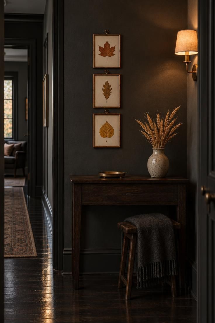 Three narrow copper and brass frames in a vertical column on a charcoal wall, each displaying a pressed autumn leaf on cream paper