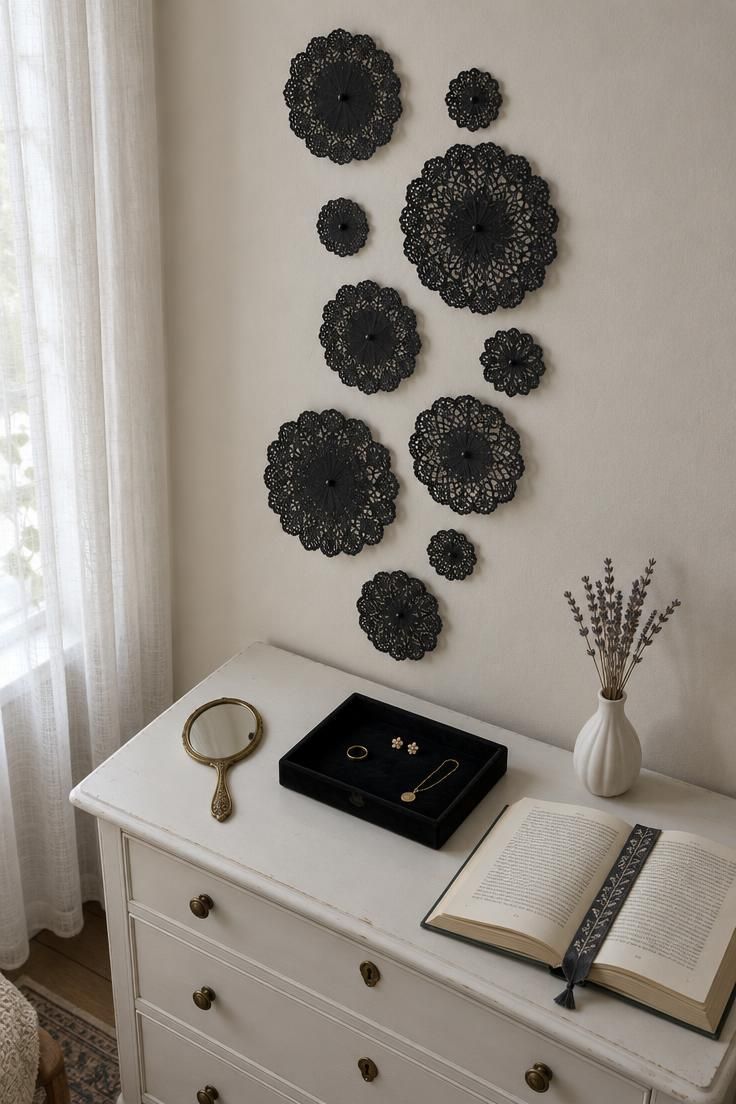 Black paper doilies in varied sizes pinned in an irregular vertical drift above a white dresser with a brass hand mirror