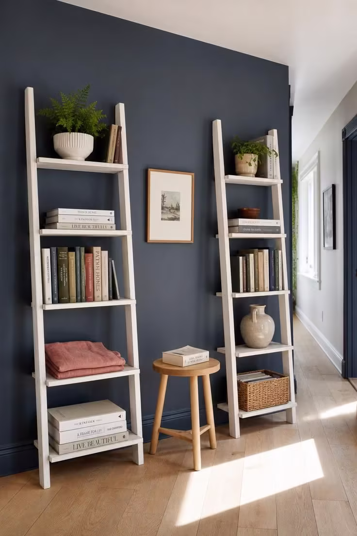 13 Charming Hallway Reading Nook Ideas for Small Homes 9 Two whitewashed ladder shelves flanking a low ash stool against a slate blue hallway wall in bright midday light.
