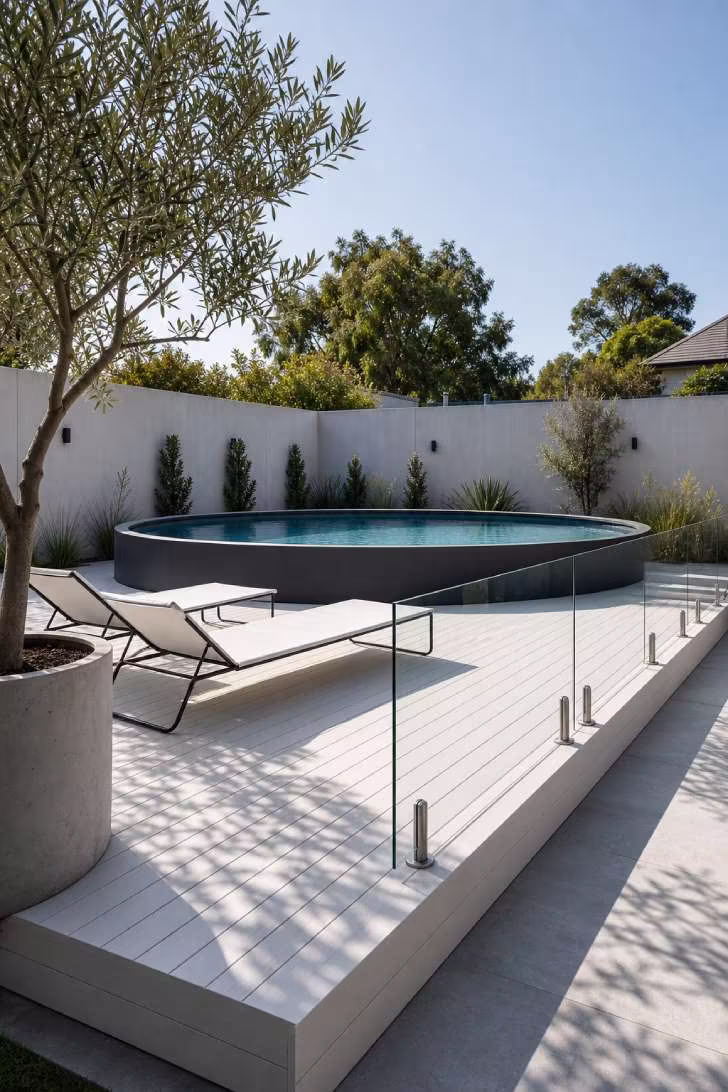 15 Nice Above Ground Pool Ideas You Can Steal This Year 3 Minimalist round above ground pool on a white composite deck with frameless glass fencing and modern loungers