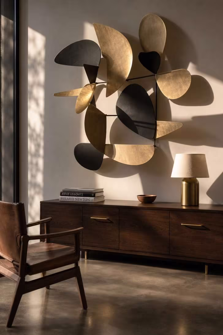 Abstract metal wall sculpture in brass and black casting shadows above a walnut console