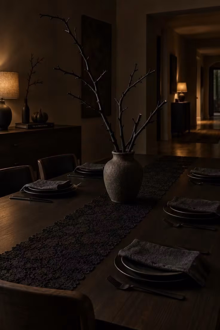 13 Indoor Halloween Decor Ideas for a Cozy October Home 8 Dark dining table with a black lace runner, matte-black painted branches in stoneware, and a bedside dresser vignette in low light.
