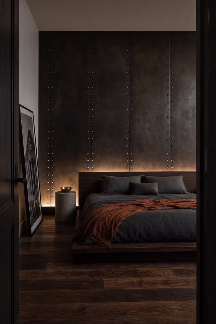 13 Bold Industrial Bedroom Ideas for a Raw Retreat 5 A riveted steel accent wall with a warm patina behind a low walnut platform bed in a moody, low-lit industrial bedroom.