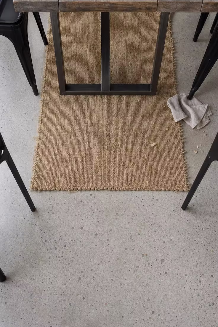 Polished concrete floor with a woven hemp runner beneath a steel-leg dining table in a cool-toned industrial dining room.