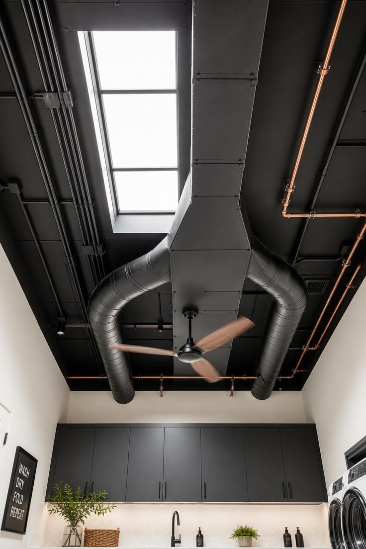 Low-angle view of exposed ceiling ductwork and pipes painted flat black with bright skylight flooding midday light