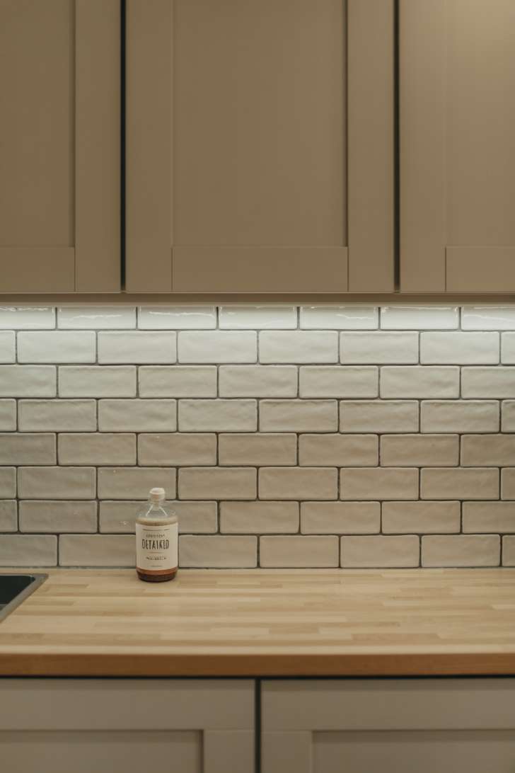 Matte off-white subway tile backsplash above a maple countertop with warm gray flat-panel cabinets in a japandi laundry room.