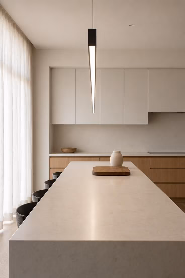 A matte black linear bar light with opal diffuser runs parallel above a waterfall-edge kitchen island.