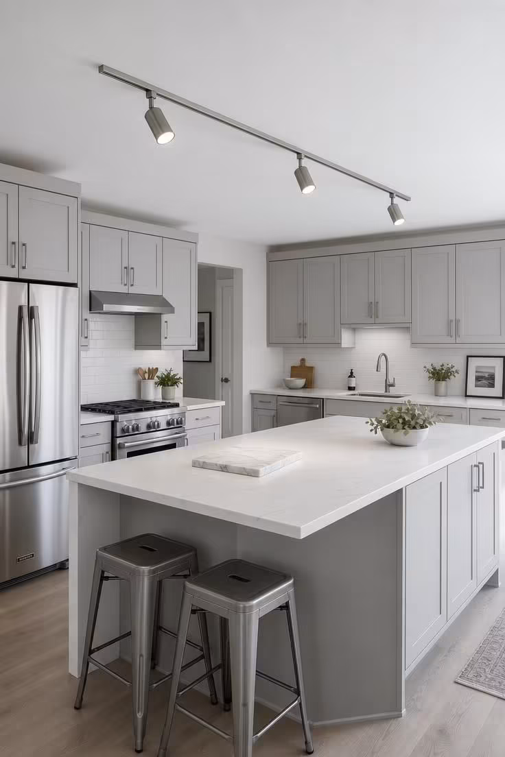 A slim brushed-nickel track with three adjustable spot heads runs parallel above a white kitchen island.