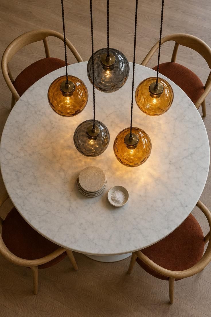 11 Cozy Kitchen Lighting Ideas Over the Table for Warmth 4 Overhead view of five hand-blown amber and gray glass pendants clustered over a round marble table.
